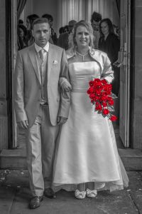 Bride and groom leaving church with stunning wedding dress and red bouquet of flowers by Resh Rall wedding photographer in Yorkshire